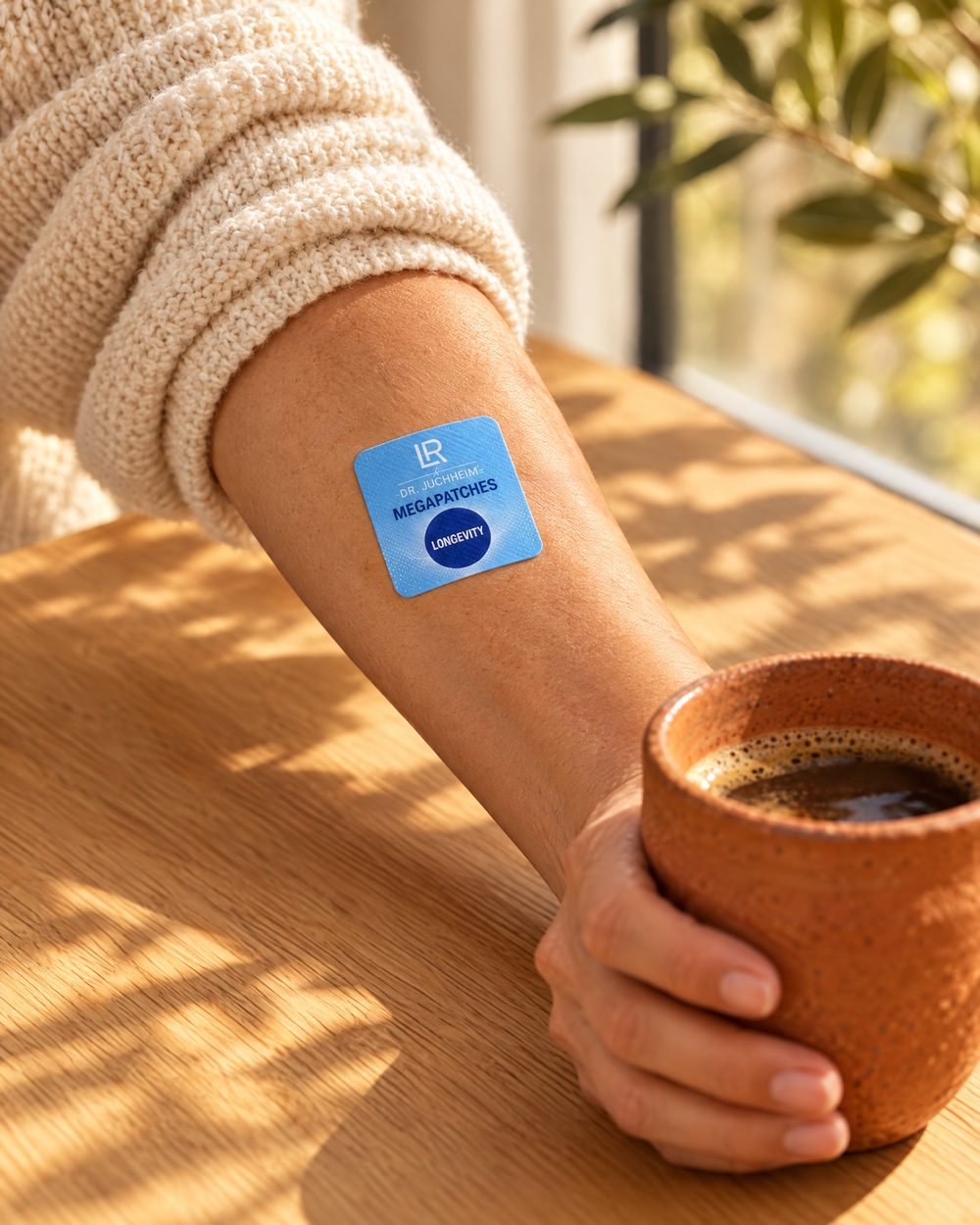 Unterarm mit aufgeklebtem blauen Mega Patch Longevity und Kaffeetasse im Morgenlicht